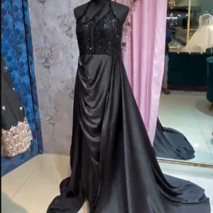 Svart glittrig lång balklänning - Elegant svart långklänning med glittrig överdel och halterneck-design. Klänningen har en vacker drapering och är perfekt för festliga tillfällen. Den skimrande ytan ger en lyxig känsla.