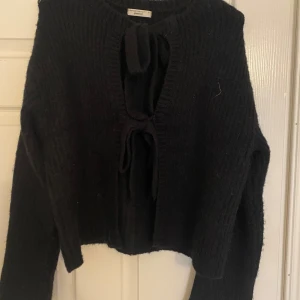 Svart stickad kofta  - Säljer en svart stickad kofta från Gina. Koftan har långa ärmar och knytband framtill som ger en unik look. Perfekt för kyliga dagar och att lägga över en topp eller klänning.