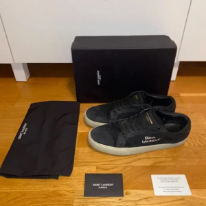 Svarta sneakers från Saint Laurent - Snygga svarta sneakers från Saint Laurent med vit sula och diskret logga på sidan. Skorna har snörning och är tillverkade i mocka. De är i storlek 43. De är använda men fortfarande i bra skick. Skriv för mer bilder och funderingar i pm.