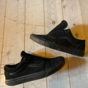 Svarta sneakers från Vans - Snygga svarta sneakers från Vans i mocka med klassisk design. Skorna har en rund tå och en robust gummisula med det ikoniska rutmönstret. Perfekta för en avslappnad stil. Skosnörena är bortplockade för en mer minimalistisk stil men går såklart att ersatta om så önskas. Använda 1-2 gånger. 
