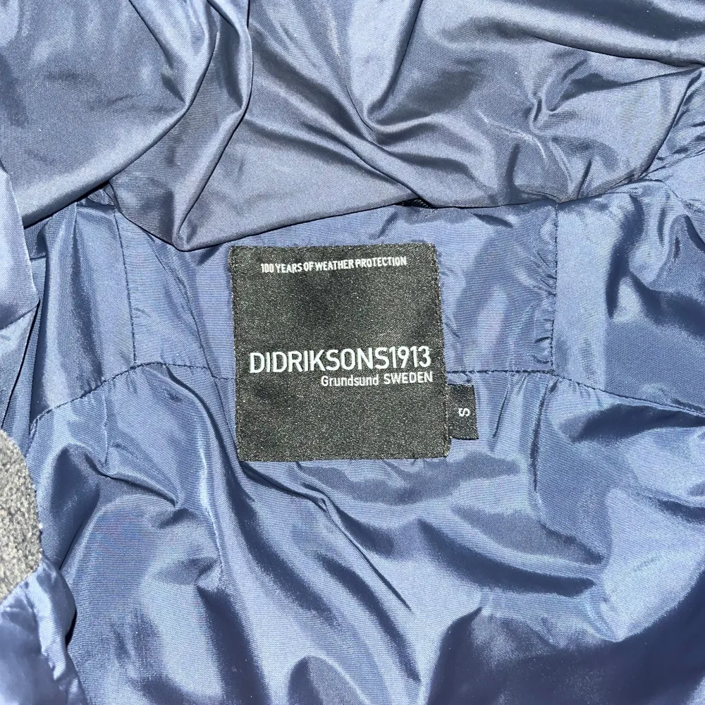 Säljer en mörkblå quiltad jacka från Didriksons med huva och dragkedja. Jackan har långa ärmar och är perfekt för kyligare väder. Den har en stilren design med diskreta detaljer och är tillverkad i syntetmaterial. Jackan är i storlek S. . Takit.