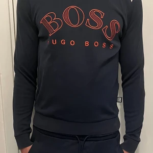 Hugo boss Set”  - Snygg mörkblå tröja från Hugo Boss med röd broderad logga på bröstet. Tröjan har långa ärmar och ribbade muddar, tröjan kostar 800kr separat, byxorna kostar 800kr separat, hela setet för 1100kr pris kan diskuteras vid snabb affär            Skriv Pm för bättre bilder!
