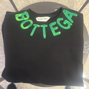 Svart tröja från Bottega Veneta - Snygg svart tröja från Bottega Veneta med gröna bokstäver på både fram- och baksidan. Perfekt för en stilren look med en touch av färg.