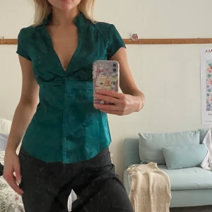 Grön blus med korta ärmar - Snygg grön blus i satin med korta ärmar och v-ringning. Blusen har en figurnära passform och knappar framtill. Perfekt för en stilren look!! Älskar men säljer då den ej passar mig i färgen💞💞💞