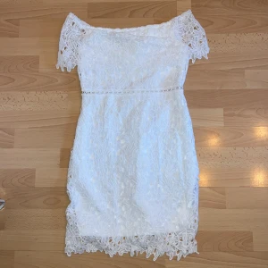 Vit spetsklänning från ElilyBazar - Säljer en vit spetsklänning från SHEIN. Klänningen har offshoulder-design och korta ärmar med vackra spetsdetaljer. Den har en dragkedja i ryggen och är i storlek S, aldrig använd