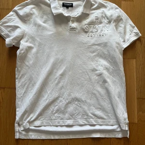 Vit kortärmad pikétröja från Tenson - Säljer en stilren vit pikétröja från Tenson med broderad text på bröstet. Tröjan har en klassisk krage med knappar och korta ärmar. Perfekt för en avslappnad och snygg look.