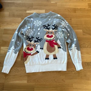 Grå jultröja med renmotiv - Säljer en grå jultröja med ett gulligt renmotiv och snöflingor. Tröjan har långa ärmar och ribbstickade muddar. Perfekt för julfirandet! 🎄