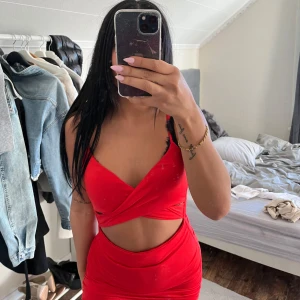 Röd omlottklänning med smala axelband - Säljer en röd, tight kortklänning med omlottdesign och smala axelband. Klänningen har en djup v-ringning och figurnära passform som framhäver siluetten. Perfekt för dig som vill sticka ut med en färgstark look.