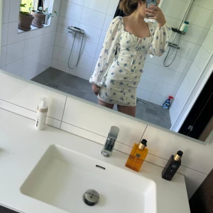 Vit blommig kortklänning med puffärmar - Säljer denna supersöta vita klänningen med blått blommönster och långa puffärmar från Hina tricot. Klänningen har knappar framtill och en söt knytning. Figurnära passform och romantisk stil, perfekt för varma dagar. Stl 34. Hör av er om ni undrar något❤️