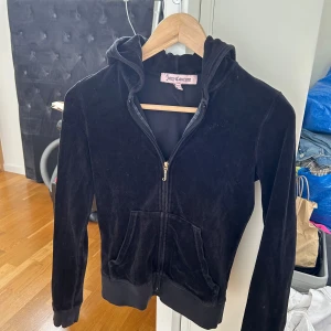 Svart velour hoodie från Juicy Couture - Säljer en klassisk svart hoodie från Juicy Couture i mjuk velour. Jackan har dragkedja framtill, huva och två fickor. Perfekt för en avslappnad och trendig look. Dam storlek s, men ganska liten och kort i modellen så tight s / xs!