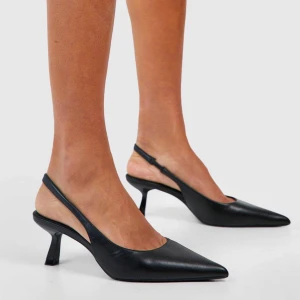 Svarta slingback pumps med klack - Stilrena svarta pumps med öppen häl och smal rem runt ankeln. Skorna har spetsig tå och medelhög klack, tillverkade i slätt skinnliknande material. Perfekta för dig som gillar en klassisk och elegant look. Perfekta att ha på klubben/fest och inte behöver vara rädd om!