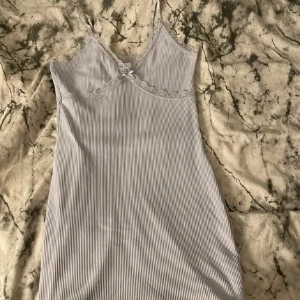 Ljuslila ribbad klänning från H&M Divided - Supersöt ljusgrå ribbad klänning från H&M Divided med spetsdetaljer och liten rosett framtill. Klänningen är ärmlös med smala axelband och har en v-ringad hals. Perfekt för en somrig look!