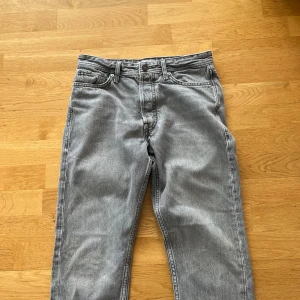 Grå jeans från Jack & Jones - Säljer ett par grå jeans från Jack & Jones i klassisk femficksmodell. Jeansen har normal passform och raka ben, med knapp- och dragkedjegylf. Perfekta för dig som gillar en enkel och stilren look. Jeansen kan lukta konstigt men det beror på att de inte är tvättade och använda på ett tag