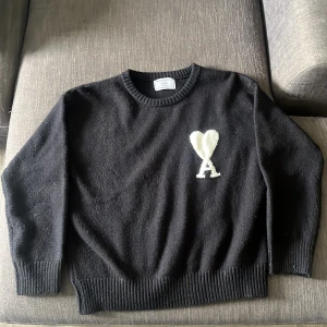 Svart stickad tröja från Ami Paris - Svart stickad tröja från Ami Paris med vit broderad logga i form av ett hjärta och bokstaven A på bröstet. Tröjan har rund halsringning och ribbade muddar vid ärmslut och nederkant. Perfekt för en stilren look. Pris kan diskuteras 