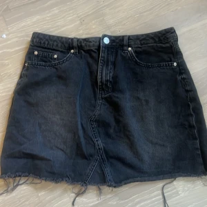 Svart jeanskjol från H&M Divided - Passar, 38 och 40 också, Svart jeanskjol från H&M Divided med klassisk femficksdesign och rå kant nertill. Kjolen har knapp- och dragkedjestängning framtill samt bakfickor. Perfekt för en cool och avslappnad stil.