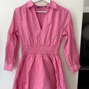 Rosa klänning med v-ringning och krage - Säljer en rosa klänning med v-ringning och  krage. Klänningen har trekvartsärm och smock i midjan. Aldrig använd💕