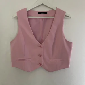 Ljusrosa väst med knappar - Snygg ljusrosa väst från Gina Tricot med v-ringning och tre knappar framtill. Västen har två dekorativa fickor och är figursydd. Den har en liten fläck på framsidan (se bild 3)💕