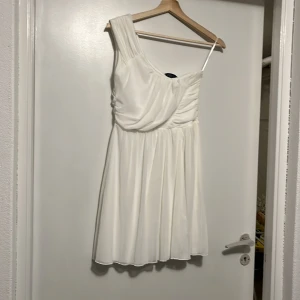 Vit one shoulder klänning från Club L - Säljer en vit kortklänning från Club L med one shoulder-design och draperad överdel. Klänningen har en luftig kjol. Perfekt för sommarens tillfällen!