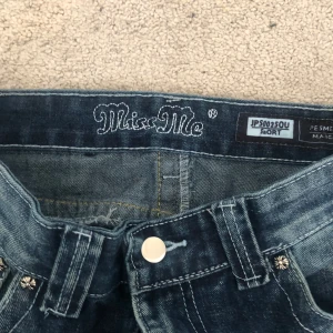Miss Me jeans med broderade bakfickor - Säljer ett par blå jeans från Miss Me med snygga broderade kors och strassdetaljer på bakfickorna. Jeansen har normal passform och bootcut-stil, klassisk femficksdesign och silverfärgade nitar. Perfekta för dig som vill sticka ut lite extra.