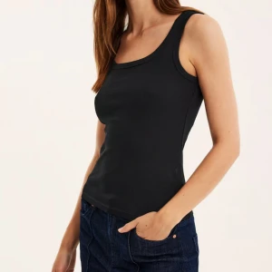 Svart ribbad linnetopp från Kappahl - Säljer en svart ribbad linnetopp från Kappahl med rundad halsringning. Toppen är ärmlös och har en tight passform, perfekt att styla till jeans eller kjol.