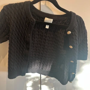 Svart stickad kofta med kort ärm och guldknappar - Säljer en svart stickad kofta med korta ärmar och snygga guldknappar från HM