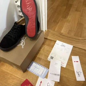 Svarta sneakers från Christian Louboutin med röd sula - Säljer ett par svarta sneakers från Christian Louboutin med ikonisk röd sula. Skorna har snörning och är tillverkade i mocka med svarta skosnören och beige insida. Kommer med originalkartong, dustbag och äkthetsbevis.