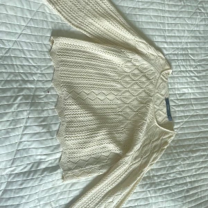 Vit stickad croppad tröja från Vero Moda - Säljer en vit stickad croppad tröja från Vero Moda med fint hålmönster och vågig nederkant. Tröjan har lång ärm och rund halsringning. Perfekt att styla med jeans eller kjol!