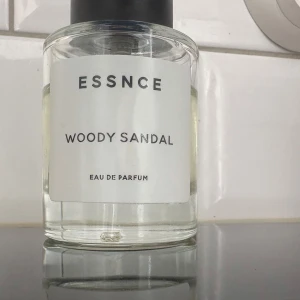 Woody Sandal Eau de Parfum från Essnce - En stilren parfymflaska med transparent glas och svart lock. Parfymen heter Woody Sandal och är en Eau de Parfum med träiga och sandelträ-noter. Bilden visar hur mycket det är kvar.