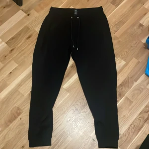 Svarta mjukisbyxor från H&M - Svarta mjukisbyxor från H&M i regular fit med dragsko i midjan. Byxorna har muddar vid bensluten och är perfekta för en avslappnad stil. Tillverkade i mjukt material för extra komfort. Storlek Large.