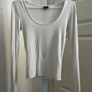 Vit långärmad topp från Gina Tricot - Säljer en enkel och stilren vit långärmad topp från Gina Tricot. Toppen har en rund, djup ringning, en slit i ärmarna och är tillverkad i ett mjukt och stretchigt material. Perfekt att styla med jeans eller kjol🌺