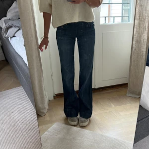 Mörkblå bootcut jeans från Direction of Choice - Säljer ett par mörkblå jeans från Direction of Choice med bootcut-passform. Storlek 34. En knappa saknas, men det syns inte när de är på. Jag är 169 cm lång, och på bilderna är mitt innerbensmått ca 82,5 cm och midjemått (platt mätt på mig) ca 31 cm.