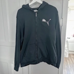 Svart PUMA huv zip-tröja 🖤 - En svart Puma zip-tröja med luva i storlek L som har några år på nacken och därmed tillkommer några defekter. Finns en fläck fram på fickan som tyvärr inte har gått bort trots alla tvättar och med fläckborttagning. Resåren nertill har vikt sig men inget jag har tänkt på när jag har haft på mig den. Det har tillkommit några hål/slitage på insidan av dragkedjan på både höger och vänster sida. FÖRST TILL KVARN!🖤(BUNDLERABATT VID KÖP AV FLER ARTIKLAR!)