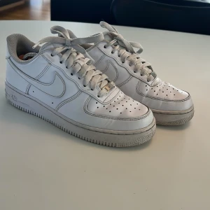 Vita Nike Air Force 1 sneakers - Klassiska vita Nike Air Force 1 sneakers med snörning och perforerade detaljer på tån. Skorna har en platt sula och är tillverkade i syntetmaterial med Nike-logga på sidan. Nypris: ca 1500 kr och mitt: 399 kr. Perfekta för en stilren och sportig look. Skriv bara om du har frågor, priset kan diskuteras!