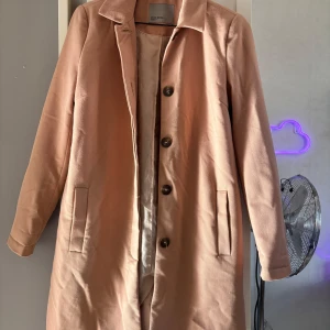Ljusrosa kappa från Zara Woman - Säljer en stilren ljusrosa kappa från Zara Woman. Jackan har klassisk krage, knäppning med tre knappar framtill och två fickor. Fodrad insida och rak passform. Perfekt för vår och höst.