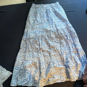 Blåvit mönstrad långkjol från Lindex - Säljer en luftig långkjol från Lindex med blått och vitt leopardmönster. Kjolen har resår i midjan för extra komfort och är perfekt för varma dagar. Tunt och skönt material som ger en avslappnad känsla.