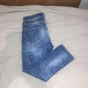 Blå jeansbyxor Pistolero 27/32 - Säljer ett par klassiska blå jeansbyxor från tiger of sweden, model pistolero med raka ben och femficksdesign. Jeansen har kontrastsömmar och normal passform. Perfekta till vardags och enkla att matcha med olika stilar.