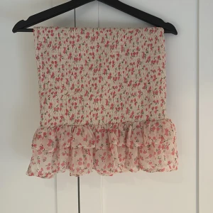 Blommig volangkjol från BikBok - Supersöt blommig volangkjol från BikBok i vitt och rosa med smockad resår och volangdetaljer både upptill och nedtill. Perfekt för sommardagar och ger en romantisk vibe med sitt lätta material och fina mönster. Går även att använda som en tubtopp om så önskas! Hör gärna av dig vid intresse💕