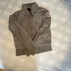 Vårjacka - Säljer en grå/oliv färgad vindjacka från Parajumpers. Jackan är nästan helt oanvänd och i nyskick. Storlek S och perfekt för sena vår och sena sommarkvällar! Luftöppningar i armhålorna för att minimera svett.