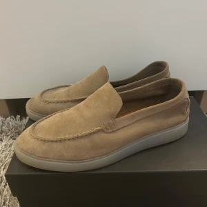 Beige mocka loafers - Säljer ett par stilrena beige loafers i mocka med rund tå och platt sula. Skorna har en enkel slip-on design utan snörning och passar perfekt till en avslappnad men snygg look. Från Massimo dutti storlek 43. Använd ett extremt fåtal ggr