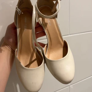 Beige pumps med ankelrem - Säljer ett par stilrena beige pumps från Anna Field med rund tå och smal klack. Skorna har en elegant ankelrem med spänne och är perfekta för dig som vill ha en klassisk look.