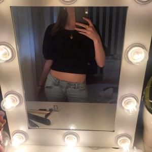 Svart croppad topp med puffärmar och öppen rygg - Säljer en svart croppad topp från Monki med puffärmar och snygg öppen rygg med knytband. Toppen har rund halsringning och är tillverkad i ett lätt, syntetiskt material. Perfekt för dig som vill ha en trendig och stilren look.