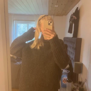 Mörkgrå stickad tröja från 157 - Mysig mörkgrå stickad tröja från 157 med grovstickad struktur och avslappnad passform. Perfekt för kyliga dagar och enkel att styla med jeans eller leggings. Rund halsringning och långa ärmar.