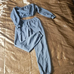 Blå croppad sweatshirt och mjukisbyxor från NLY Trend - Säljer ett set med croppad långärmad sweatshirt och matchande mjukisbyxor i ljusblått från NLY Trend. Båda delarna har resår i midja och ärmslut/ben, vilket ger en skön och avslappnad passform. Perfekt för chill dagar eller när du vill vara bekväm.