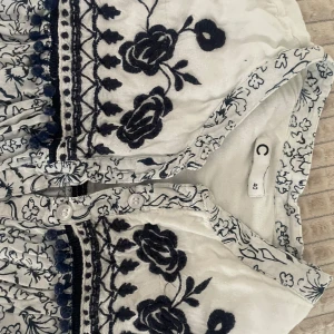 Vit och marinblå blommig blus från C - Superfin vit blus med marinblå broderade blommor och detaljer. Blusen har knappar framtill, v-ringning och ett vackert blommönster över hela tyget. Perfekt för sommarens alla tillfällen!Pris kan diskuteras och köparen står för frakten💕