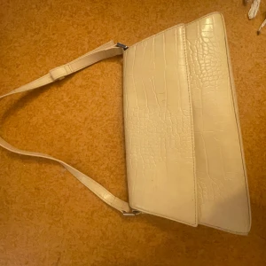 BEIGE VÄSKA - Snygg beige axelväska med justerbar rem och krokodilpräglat mönster. Väskan har en stilren design och är perfekt för att bära dina nödvändigheter med stil. Passar till många olika tillfällen. Lite fläckig men går bort kan tvättas💞💞
