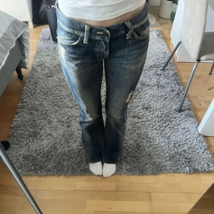 Blå jeans med slitningar - Säljer ett par blå jeans med slitningar och bootcut-stil. De har en låg midja och klassiska femficksdetaljer. Perfekta för en avslappnad look. Aldrig använda endast provade🤗