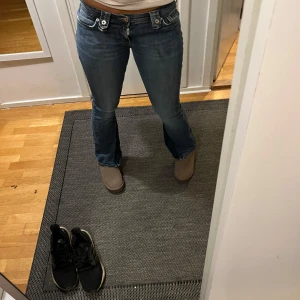 Vintage Blå jeans från Dolce & Gabbana - Snygga blå jeans från Dolce & Gabbana med låg midja och bootcut-stil. Byxorna har dekorativa knappar och dragkedja framtill.  Midjemått rakt över: 40cm                   Innerbenslängd: 76 cm