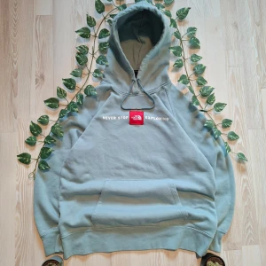 Grå hoodie från The North Face - Säljer en grå hoodie från The North Face med texten 'Never Stop Exploring' tryckt på bröstet. Den har en stor ficka framtill och justerbar huva med snören. Perfekt för kyliga dagar!