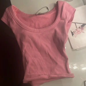 Rosa ribbad kortärmad topp - Säljer en söt rosa ribbad topp med korta ärmar. Perfekt för en avslappnad stil. Toppen har en rund halsringning och är gjord i ett mjukt material.