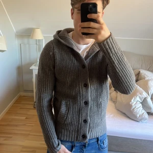 Hartford grå cardigan - Säljer en stilren grå cardigan från Hartford. Storlek L men sitter som M. Den är tillverkad i 80% lammull och 20% nylon, vilket gör den både varm och bekväm. Koftan har en huva och knappar framtill, perfekt för kyligare dagar. Passar bra till ett par feta jeans. Skick 8/10 tröjan är lite nopprig på armarna. Skriv för frågor eller mer bilder🙌🤩
